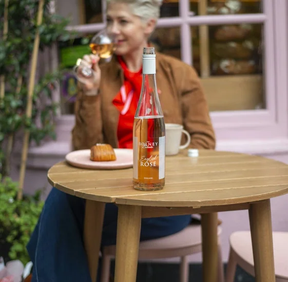 A bottle of Bolney Estate English Rosé on a table, with a woman tasting wine in the background