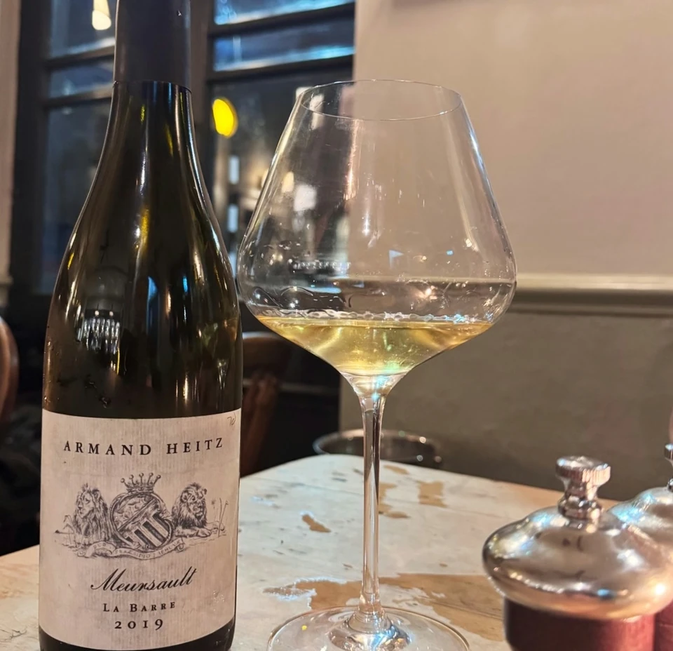 Armand Heitz Meursault bottle beside a glass of pale wine on a restaurant table