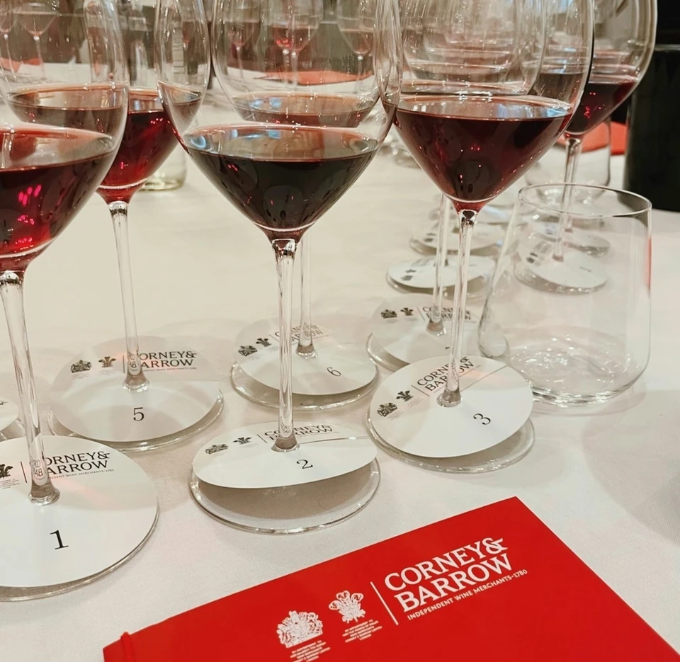 Numbered wine glasses filled with red wine beside a red Corney & Barrow booklet