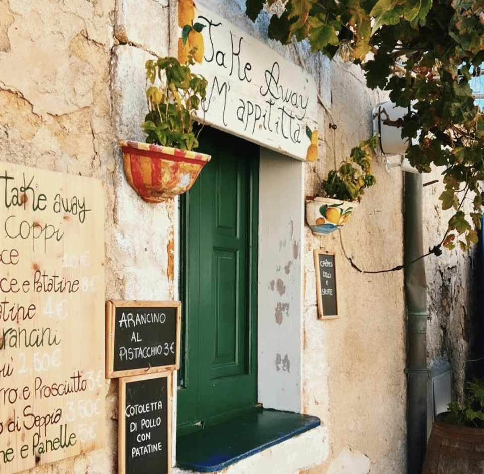 Rustic Sicilian takeaway doorway with a green door, handwritten food menus and grapevines overhead