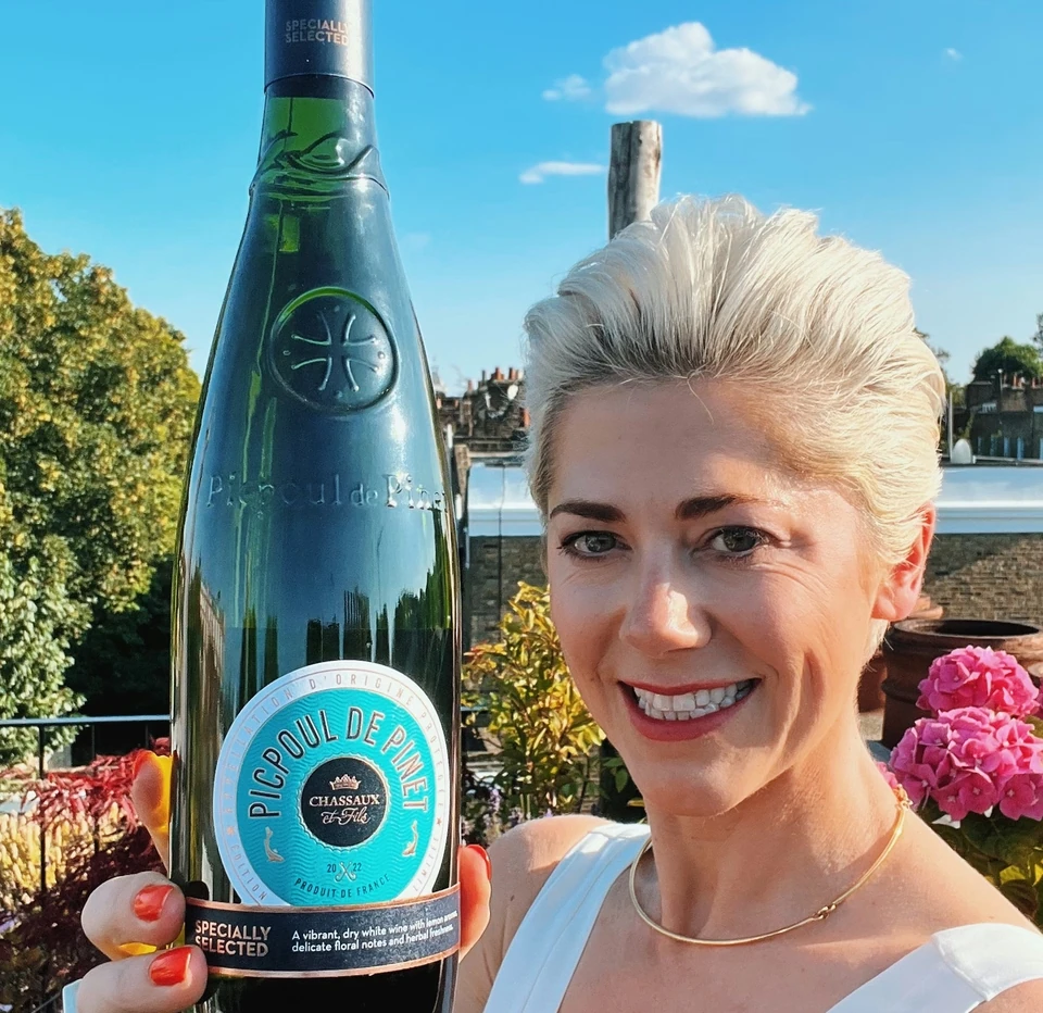 Woman holding a bottle of Picpoul de Pinet wine outdoors