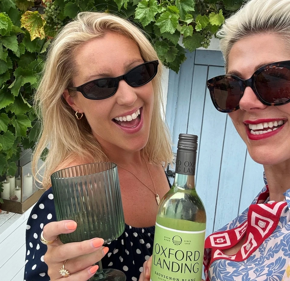 Two women holding a glass and an Oxford Landing Sauvignon Blanc bottle among grapevines