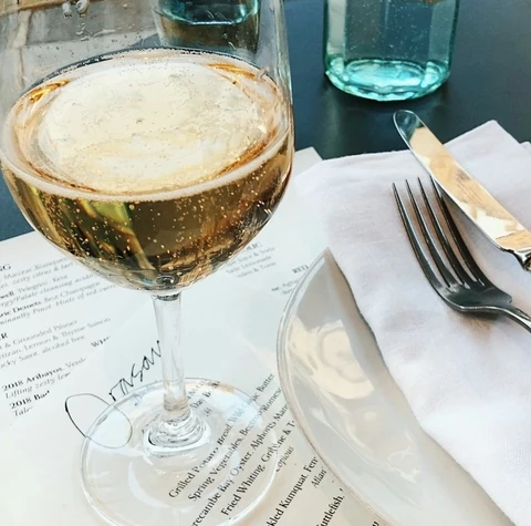 Glass of sparkling wine beside a menu, water bottle and folded napkin