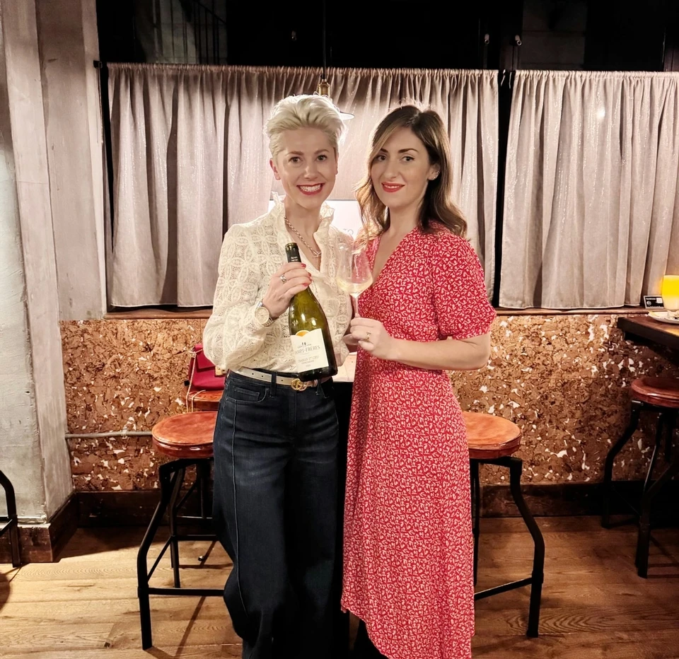 Two women holding a Chablis bottle and wine glass at a tasting