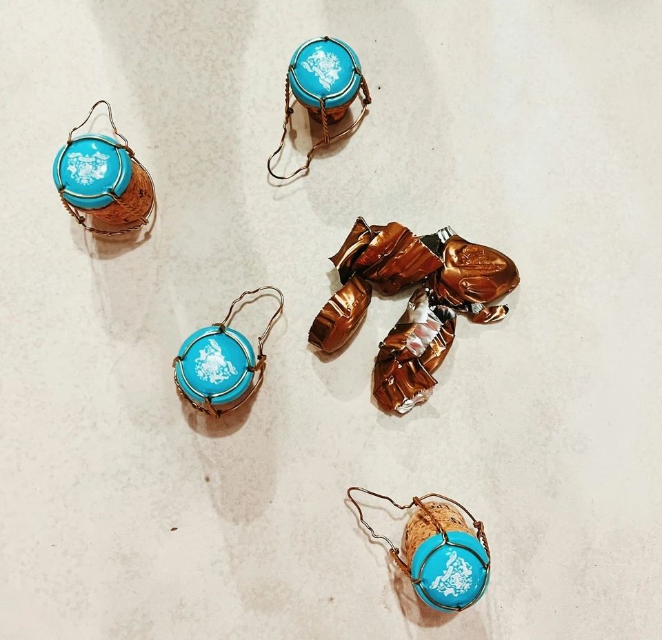 Four turquoise-topped sparkling wine corks and crumpled copper foil on a pale surface