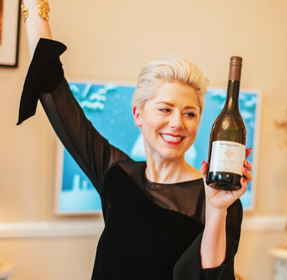 Woman raising one hand while holding a bottle of Pajzos Tokaj dry white wine