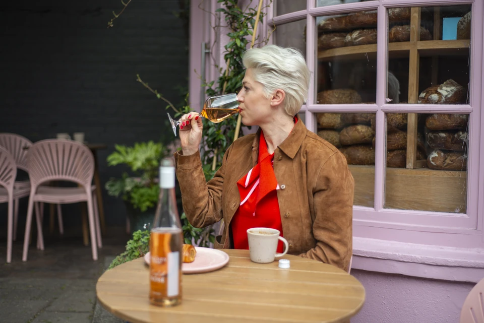 Person tasting Bolney rosé at an outdoor café table beside a pink bakery window