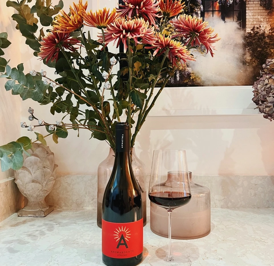 Animardente Etna red wine beside a filled glass and a vase of autumn flowers