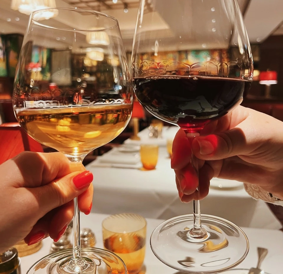 Two hands hold glasses of white and red wine over a restaurant table