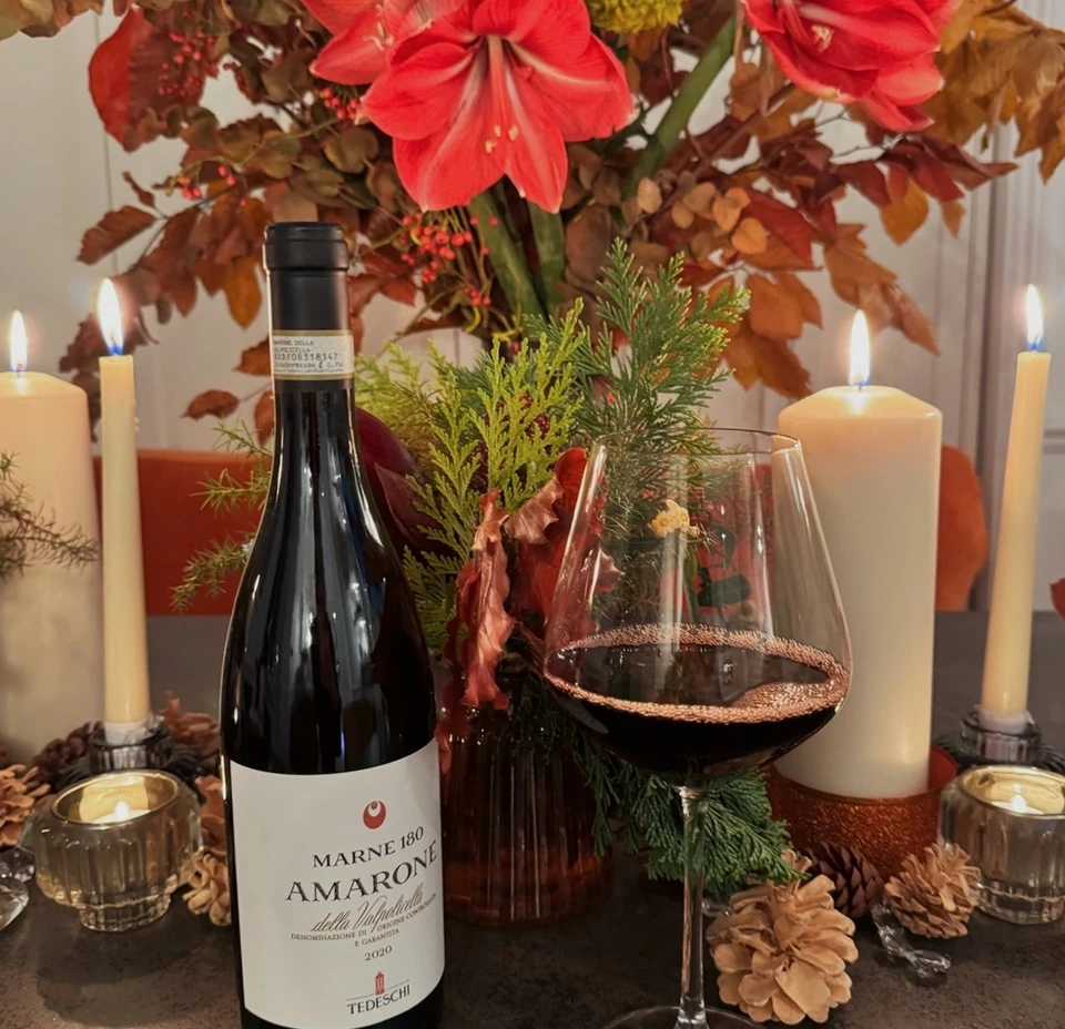 Tedeschi Amarone della Valpolicella bottle and a glass of red wine beside candles and flowers