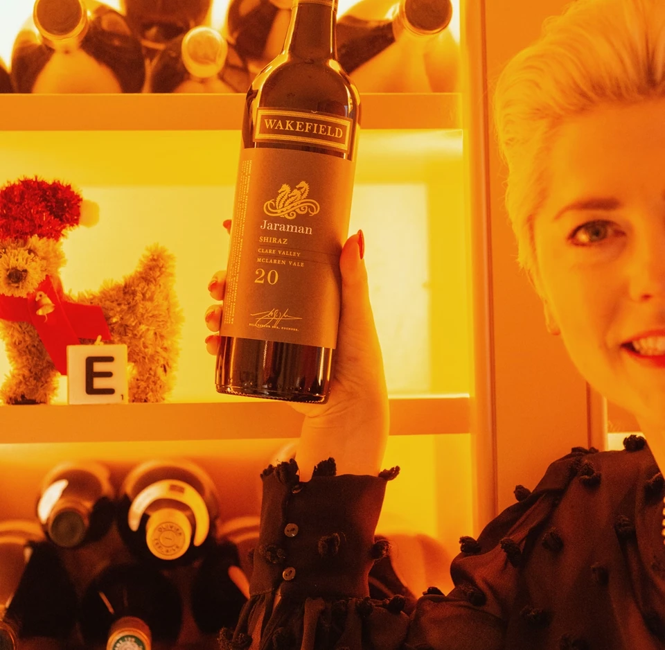 Person holding a Jaraman Shiraz wine bottle in front of a wine display