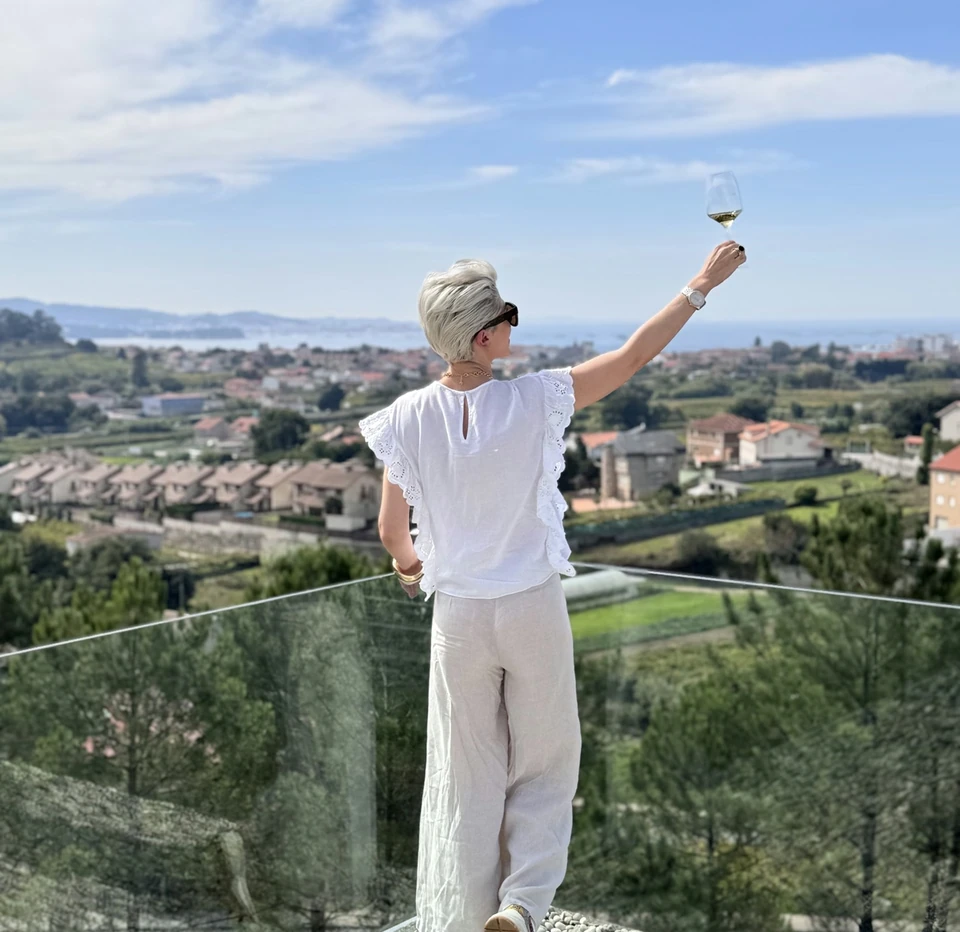 Person raising a glass of white wine overlooking a coastal landscape