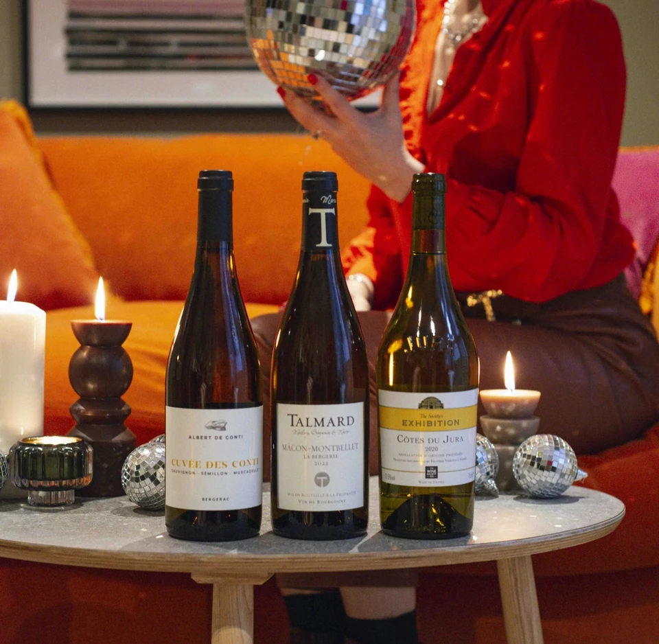 Three wine bottles on a candlelit table with disco balls and a person in a red blouse