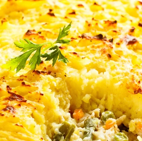 Fish pie with peas, carrots and parsley in a white baking dish