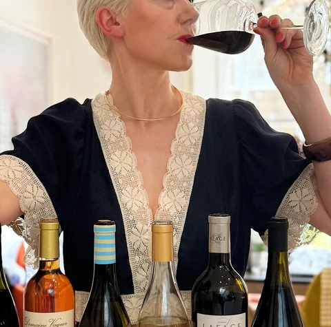 Woman tasting red wine behind a row of Languedoc wine bottles