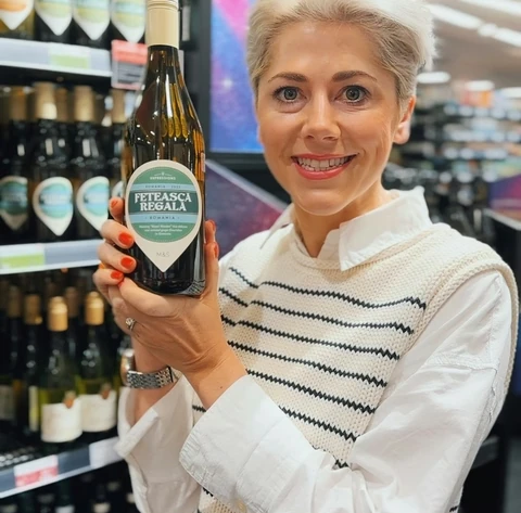 Woman holding a bottle of Petească Regală wine in a shop