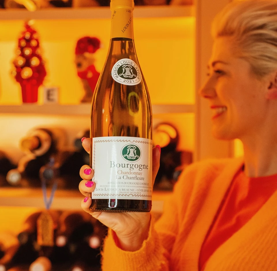 A Bourgogne Chardonnay bottle held in front of illuminated wine shelves