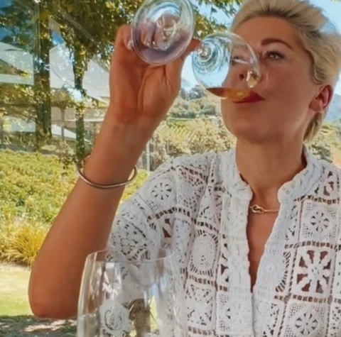 Woman tasting pale wine from a glass outdoors beside a vineyard