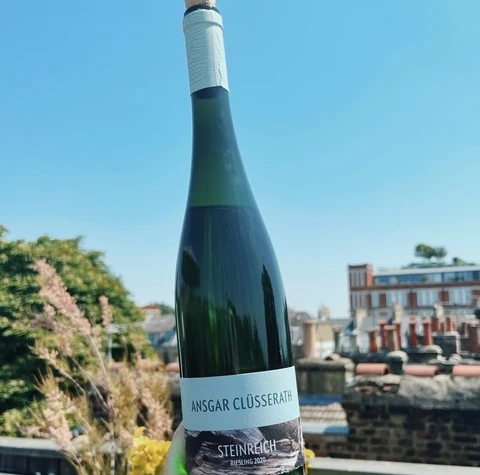Hand holding an Ansgar Clüsserath Steinreich Riesling 2020 bottle against a sunny rooftop backdrop