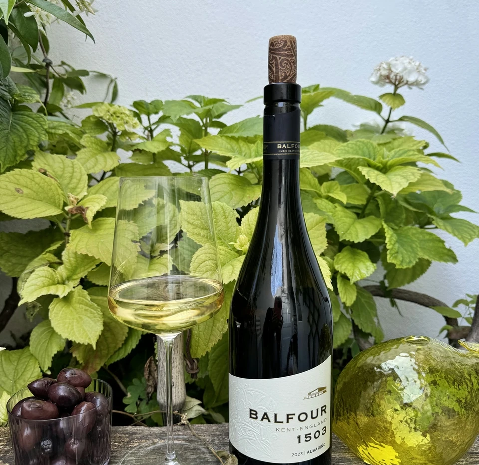 Bottle of Balfour 1503 Albariño with a glass of wine, olives and garden foliage