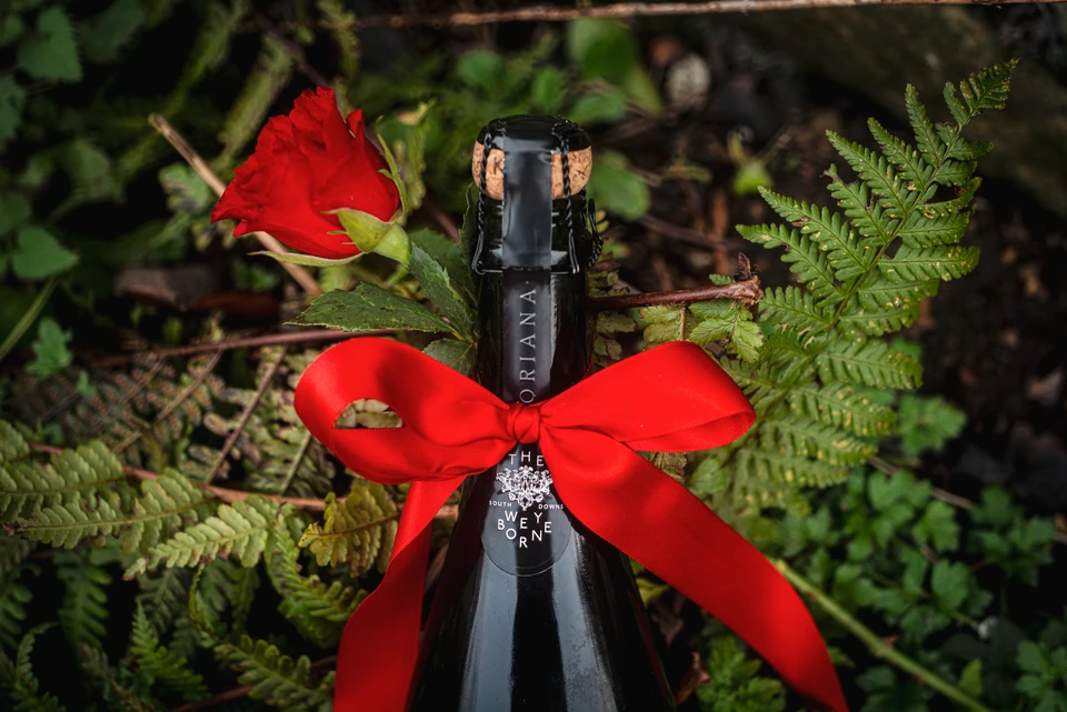 Weyborne sparkling wine bottle with a red bow and rose among green foliage
