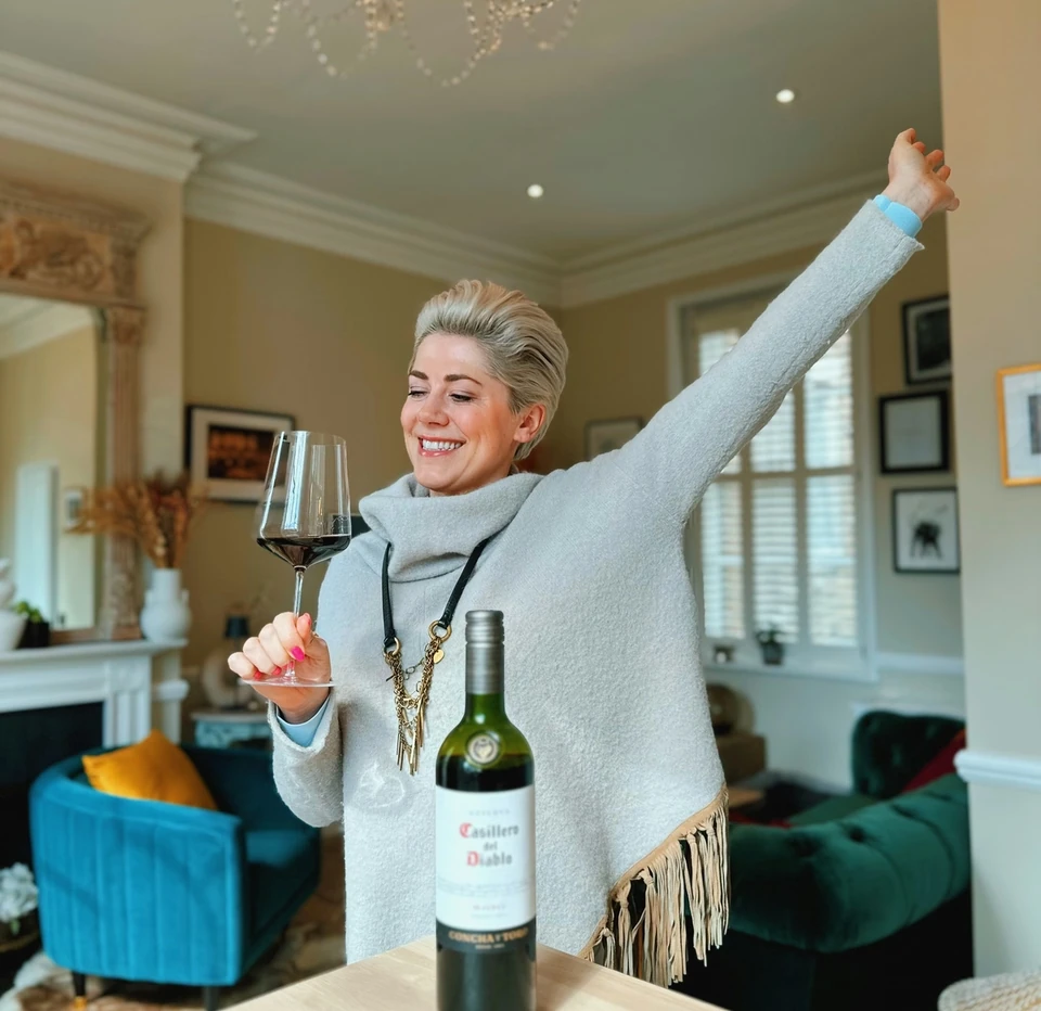 Woman raising an arm while holding a glass of red wine beside a bottle of Malbec