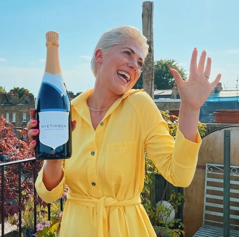 Woman in a yellow dress holding a Nyetimber sparkling wine bottle outdoors
