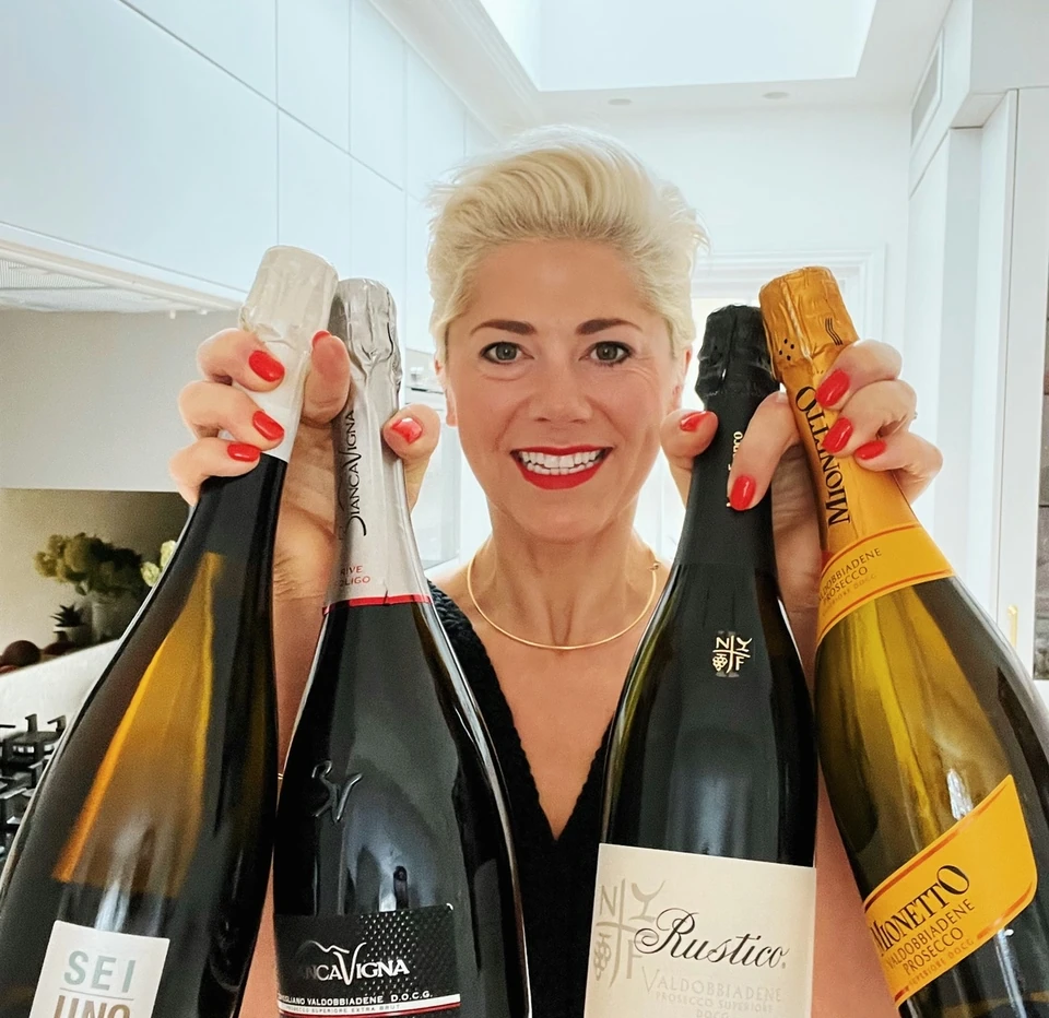 Four Prosecco bottles held up in a bright kitchen