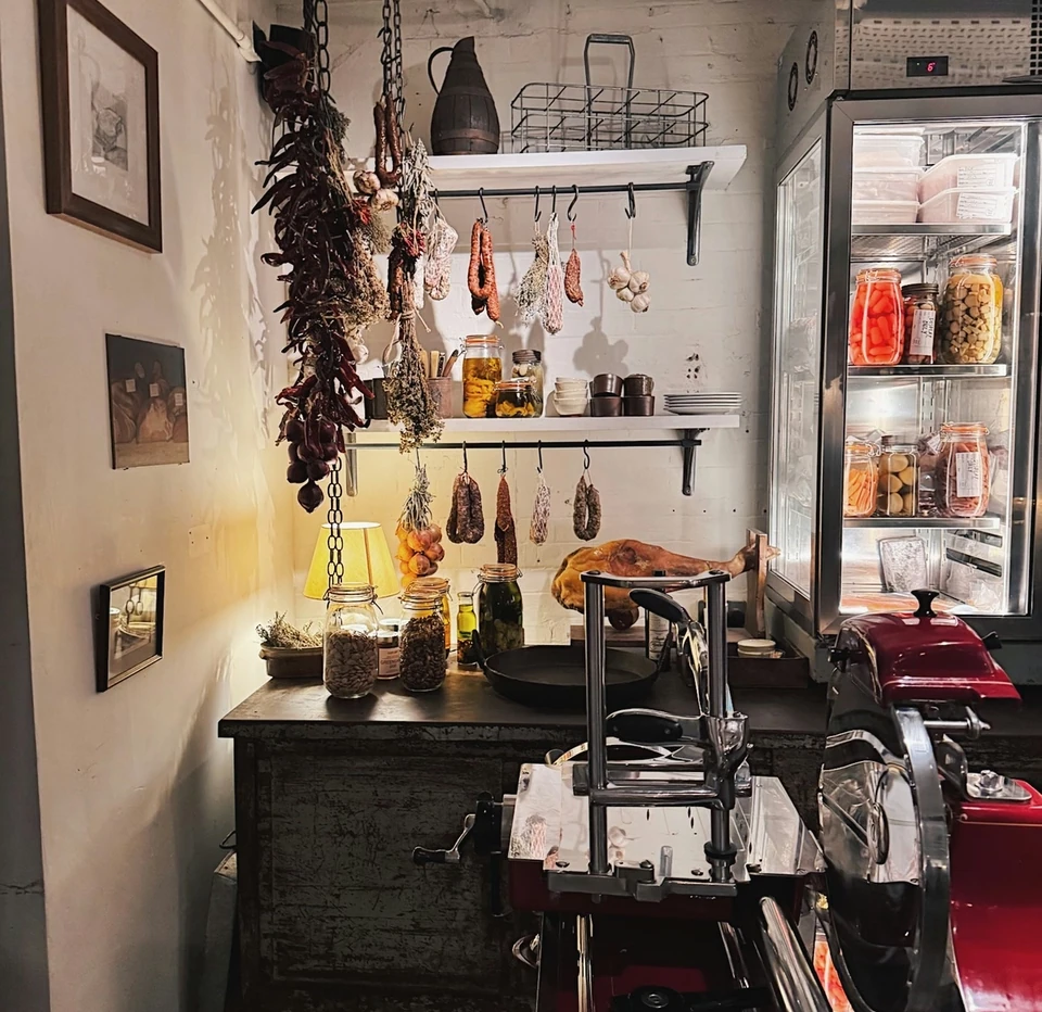 Farm shop interior with hanging cured meats, jars of preserves and a red Berkel slicer