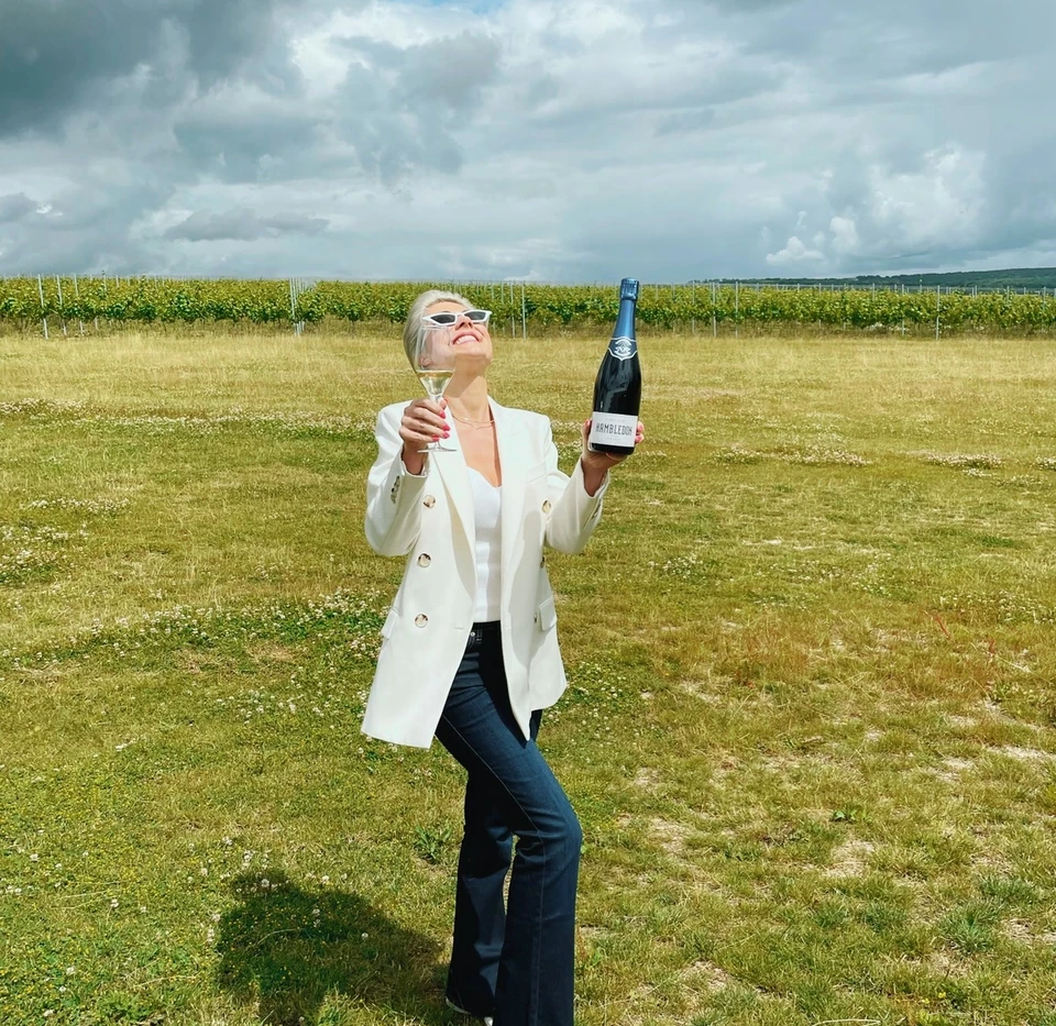 Person holding a glass of sparkling wine and a Hambledon bottle in a vineyard