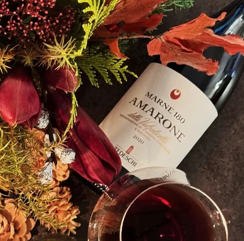 Tedeschi Amarone bottle, red wine, flowers and a candle on a table