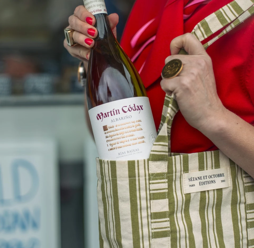 Person in a red top and striped apron holding a bottle of Martín Códax Albariño