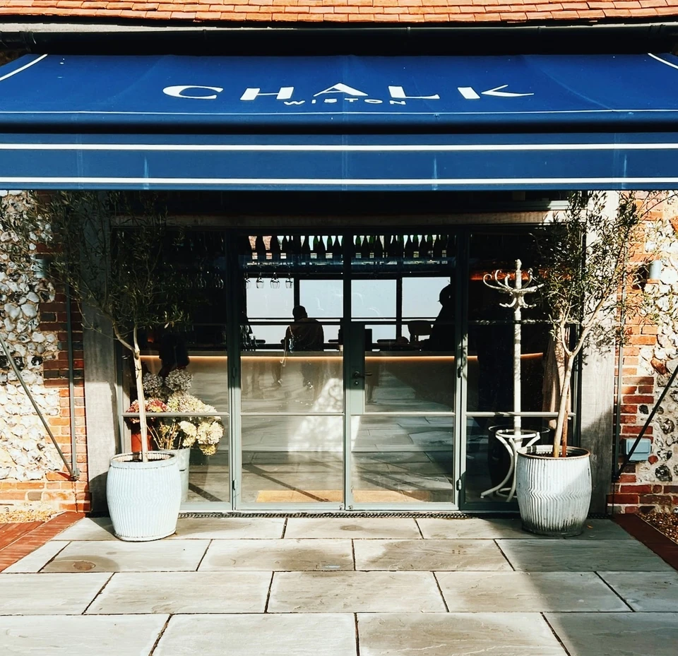 Entrance to Wiston's Chalk venue with a blue awning, glass doors and potted trees