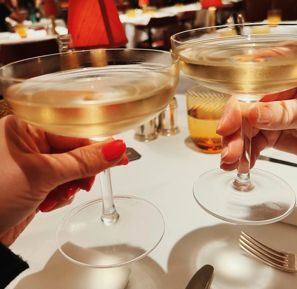 Two coupe glasses of pale sparkling wine held above a restaurant table at The Colony Grill Room