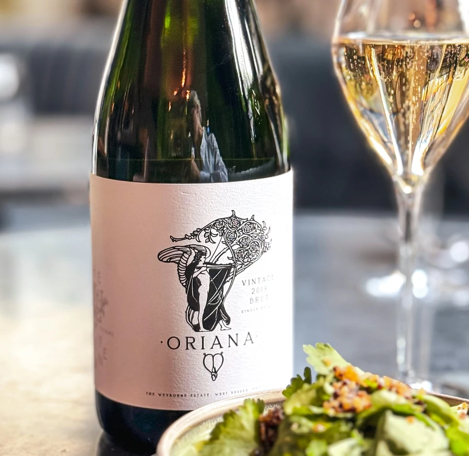 Weyborne Oriana sparkling wine beside a filled glass and salad