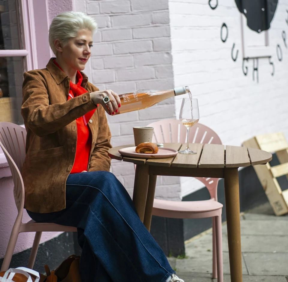 Person pours Bolney rosé into a glass beside a pastry on an outdoor café table