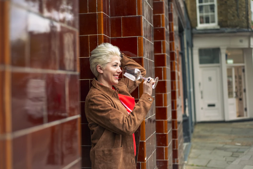 Elizabeth Hawthornthwaite holds a wine glass beside a tiled London building.