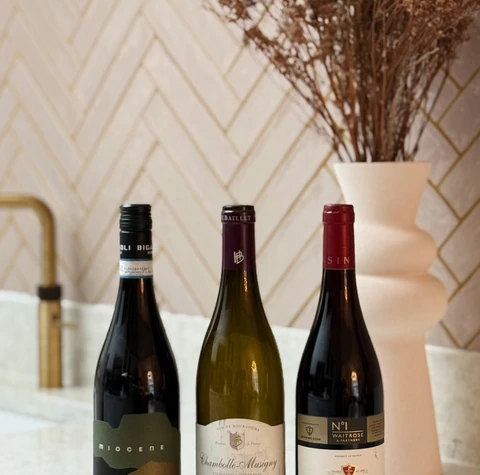 Three red wine bottles, including Beaujolais-Villages, on a kitchen worktop beside dried flowers