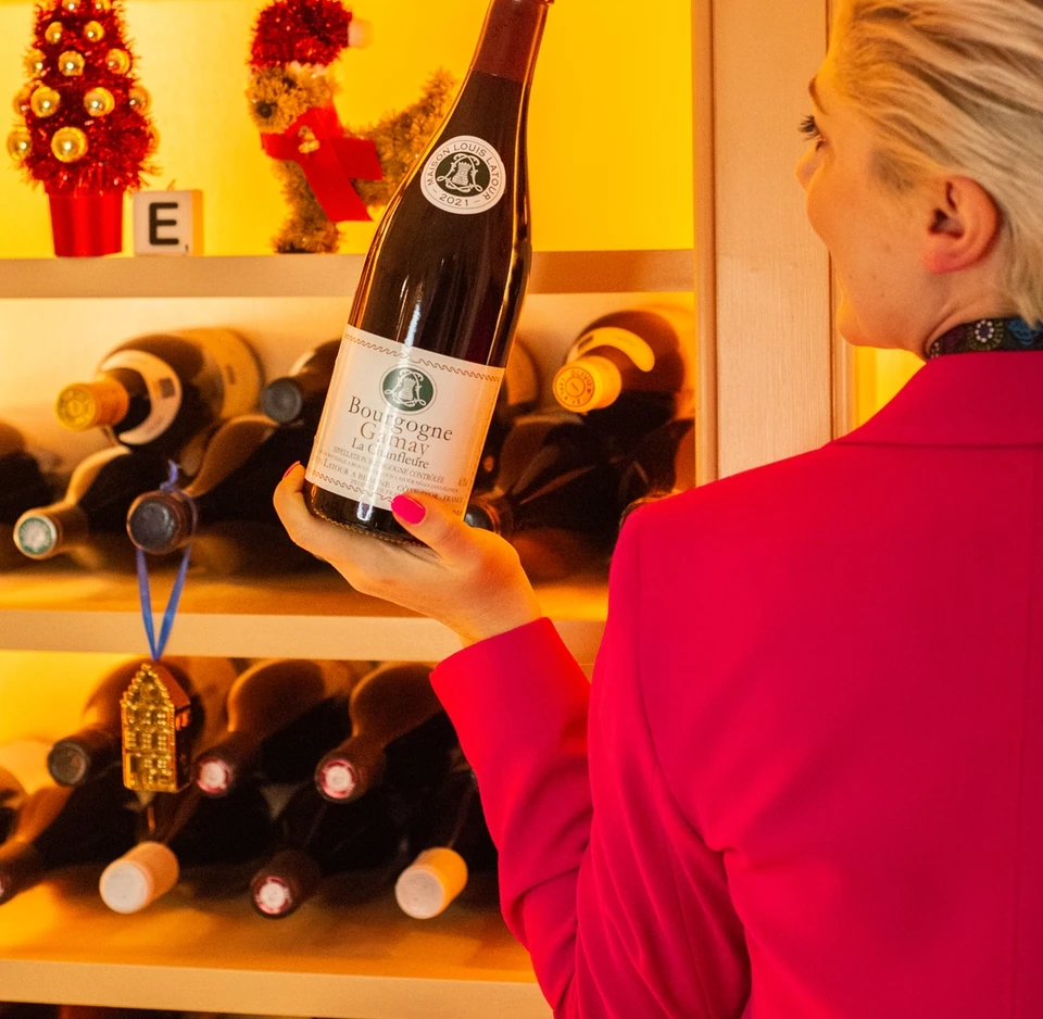 Woman holding a bottle of Bourgogne Gamay in front of a wine rack