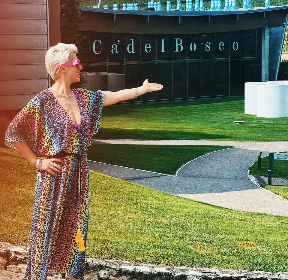 Woman gesturing towards the Ca' del Bosco winery building and landscaped grounds