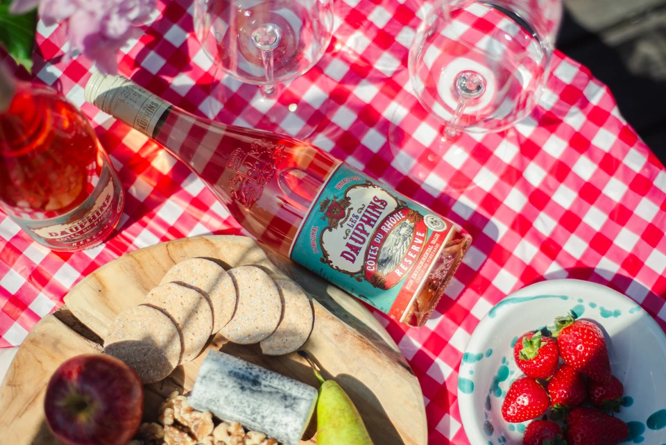Les Dauphins rosé with glasses, cheese, biscuits, fruit and a red checked tablecloth