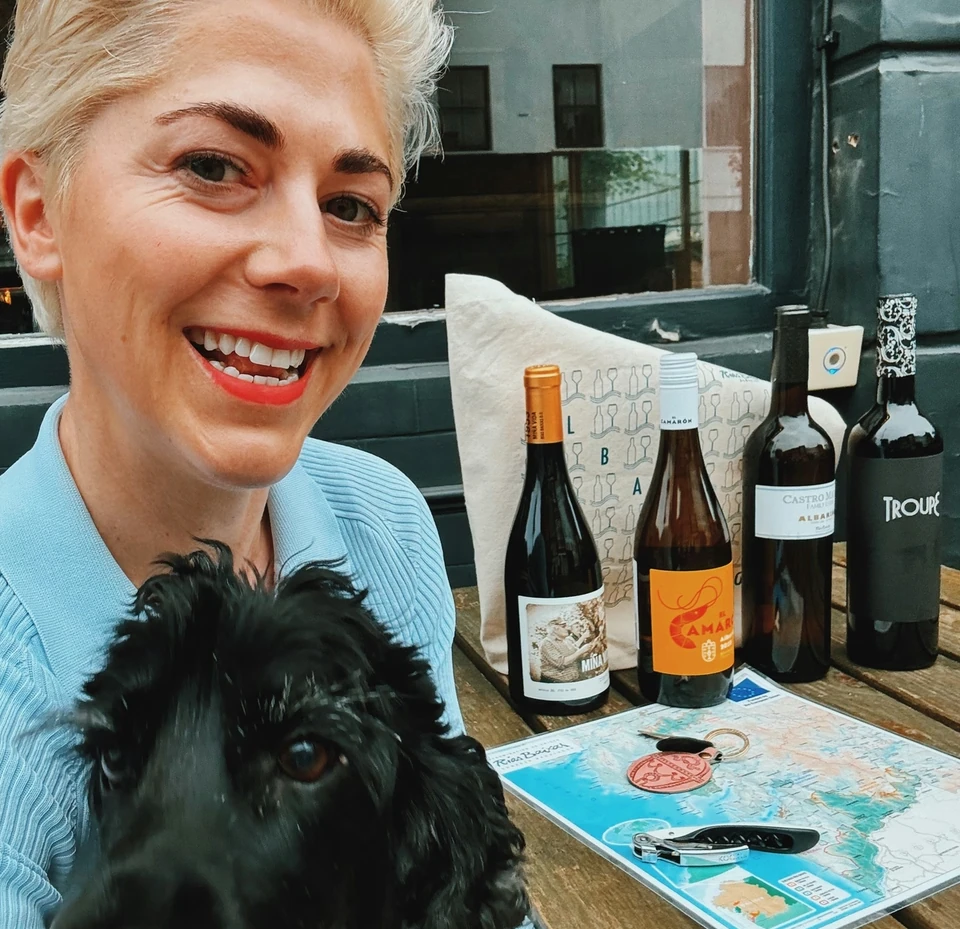 Elizabeth holding a black dog beside four Rías Baixas wine bottles and a map