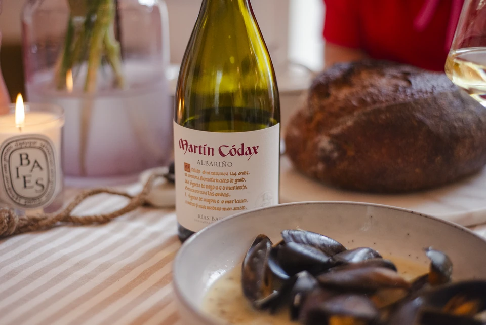 A bottle of Martin Codax Albariño beside mussels, bread and a lit candle
