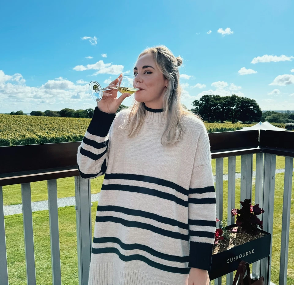 Woman tasting sparkling wine on a balcony overlooking a Gusbourne vineyard