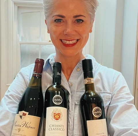A woman holds three bottles of red wine, including a bottle of Barbera d'Asti