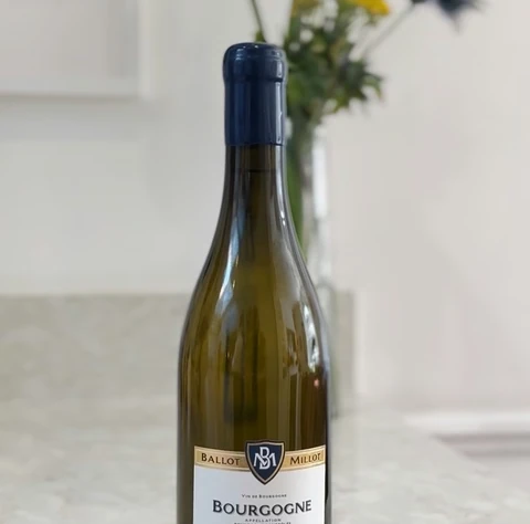 Bottle of Ballot-Millot Bourgogne Chardonnay 2019 on a marble surface with flowers behind it