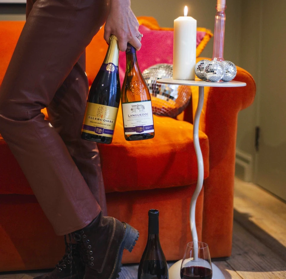 Sainsbury's English sparkling and red wine bottles beside candles and a velvet chair