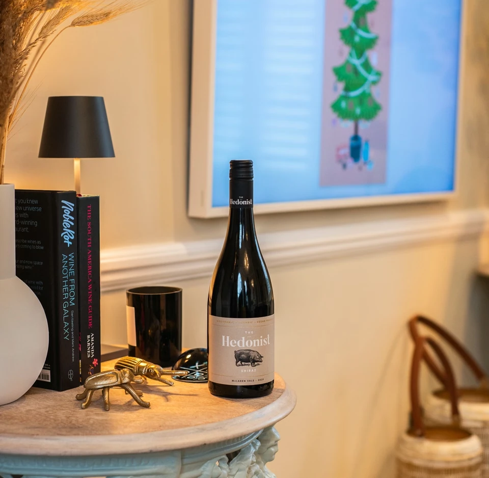 The Hedonist Shiraz bottle displayed on an ornate table in a warmly lit interior
