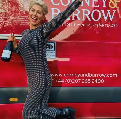Woman holding a wine bottle beside a red Corney & Barrow vehicle