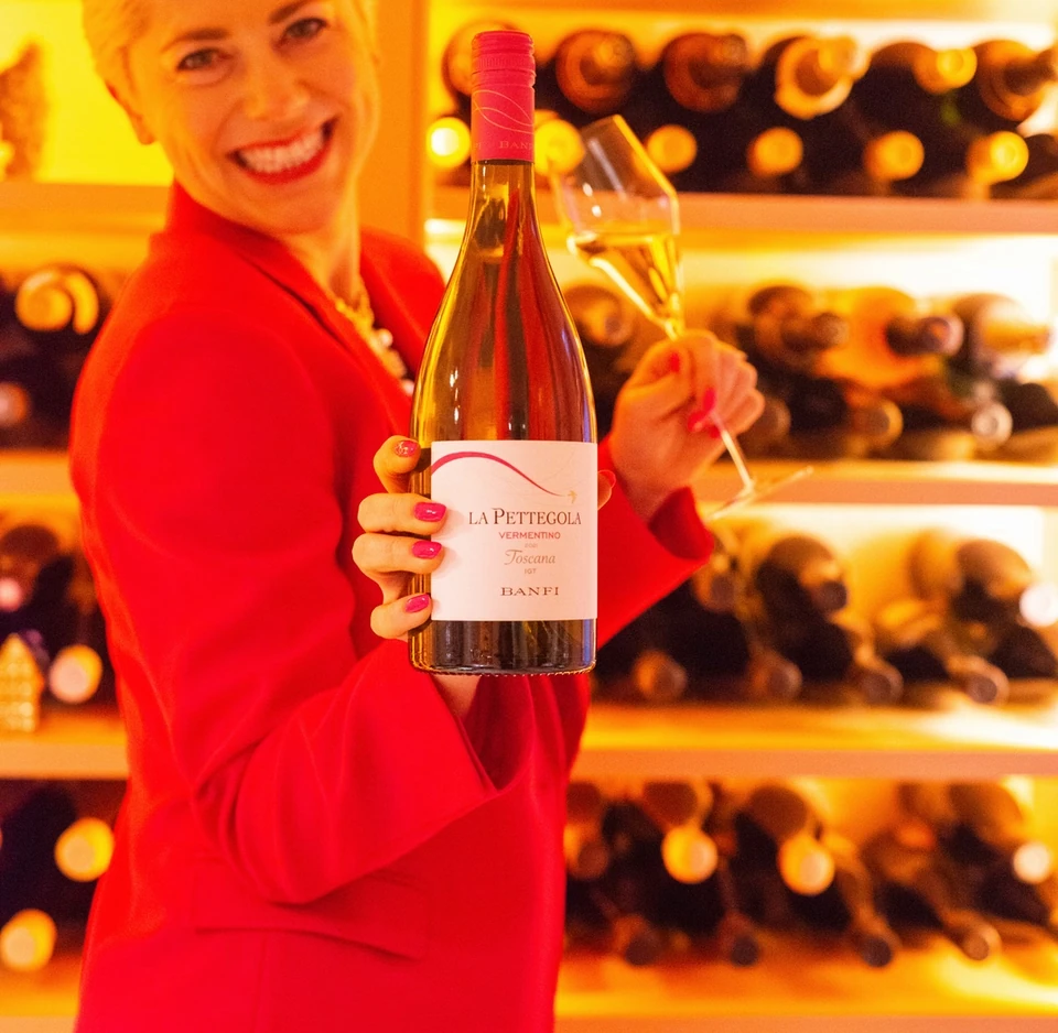 Woman holding a bottle of La Pettegola Vermentino in front of wine shelves